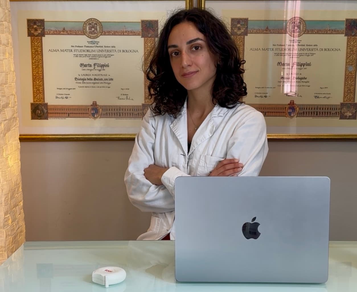 Marta Filippini in camice nello studio, davanti ai diplomi di laurea